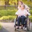 Young woman leaning in close behind an aging adult in wheelchair in a park.