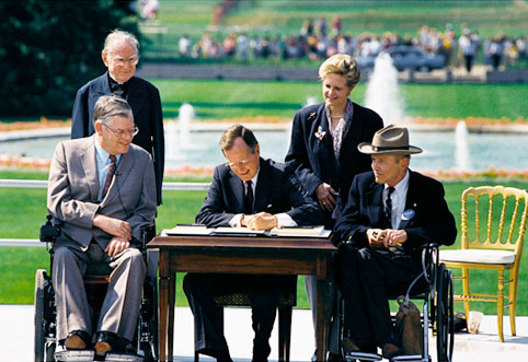 President George H. W. Bush signs the Americans with Disabilities Act of 1990 into law. Pictured (left to right): Evan Kemp, Rev Harold Wilke, Pres. Bush, Sandra Parrino, Justin Dart. President Bush signs the Americans with Disabilities Act on the White House South Lawn on July 26, 1990. The act prohibited employer discrimination on the basis of disability. Date: July 26, 1990. Permission details: Public Domain