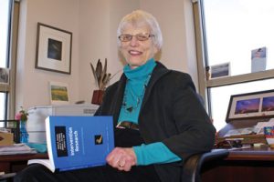 Maeda Galinsky, Ph.D., sitting in her office holding one of the books she published on social work intervention.