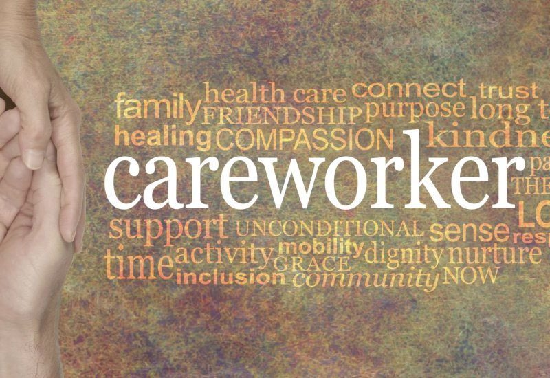 female hands gently cupped around male cupped hands beside the word CAREWORKER surrounded by a relevant word cloud on a rustic stone background