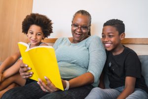 Portrait of African American grandmother reading a book to children at home. 
